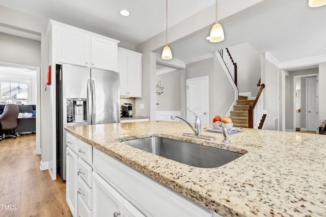 kitchen featuring pendant lighting, light stone counters, light wood-style floors, white cabinets, and a sink