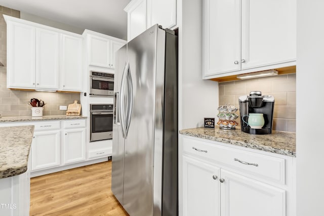 kitchen featuring light stone counters, light wood-style flooring, white cabinets, appliances with stainless steel finishes, and tasteful backsplash