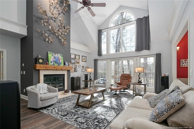 living area featuring high vaulted ceiling, a ceiling fan, wood finished floors, a glass covered fireplace, and baseboards