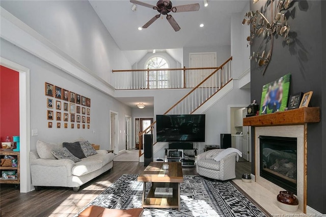 living room with a fireplace with flush hearth, a ceiling fan, wood finished floors, a high ceiling, and stairs