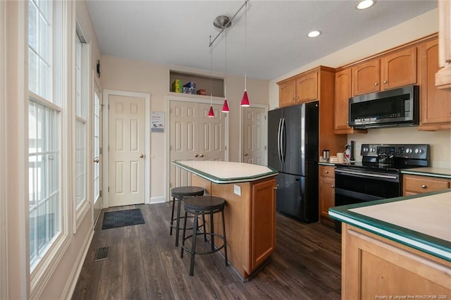 kitchen featuring a kitchen island, a breakfast bar, dark wood finished floors, black appliances, and pendant lighting