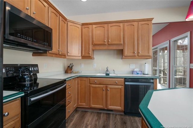 kitchen featuring dark wood-type flooring, light countertops, vaulted ceiling, black appliances, and a sink