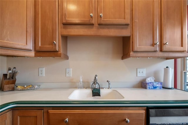 kitchen with a sink, dishwashing machine, brown cabinetry, and light countertops