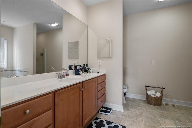 bathroom featuring toilet, vanity, a shower stall, and baseboards