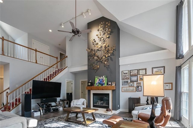 living room featuring stairway, wood finished floors, high vaulted ceiling, and a glass covered fireplace