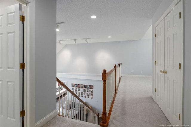 hallway with an upstairs landing, baseboards, carpet floors, and a textured ceiling