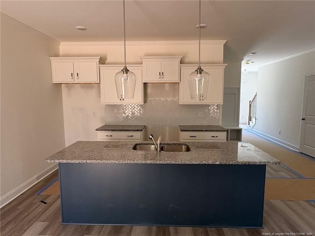 kitchen featuring a sink, ornamental molding, an island with sink, white cabinets, and tasteful backsplash