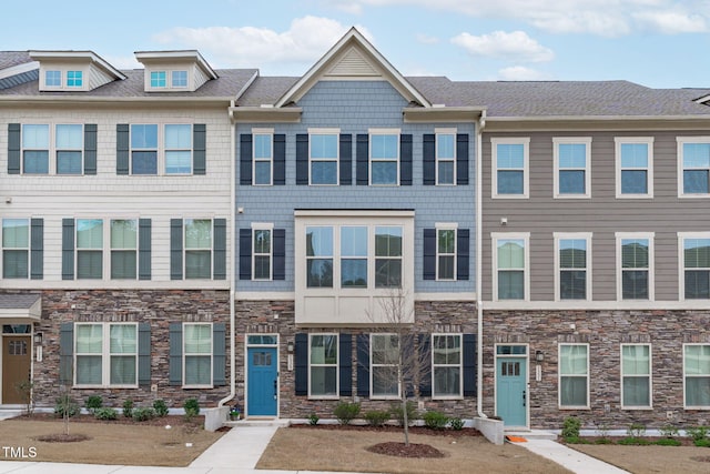 townhome / multi-family property with stone siding and a shingled roof