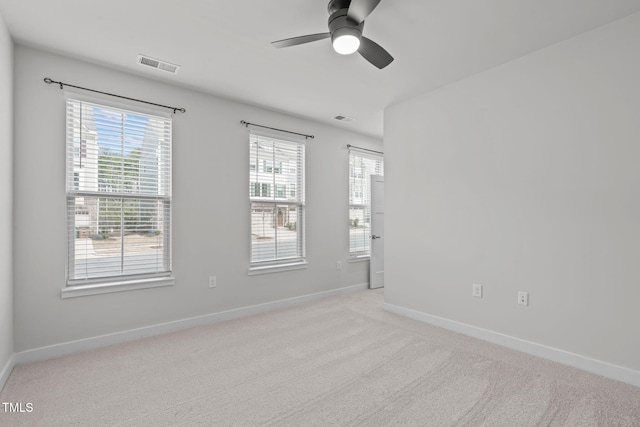 empty room with a wealth of natural light, visible vents, light colored carpet, and a ceiling fan