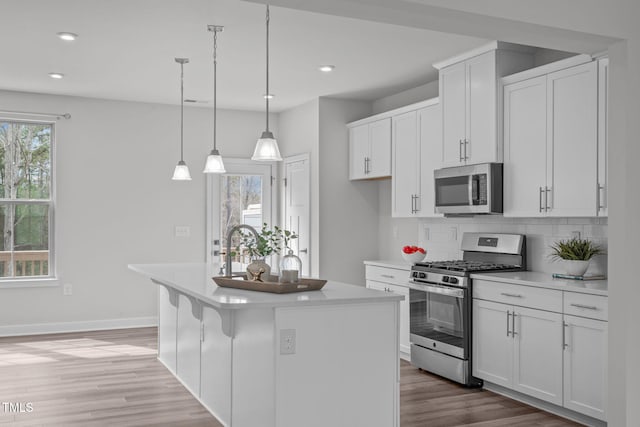 kitchen featuring a healthy amount of sunlight, a center island with sink, light wood-style flooring, appliances with stainless steel finishes, and tasteful backsplash