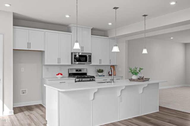 kitchen with a center island with sink, light countertops, decorative backsplash, appliances with stainless steel finishes, and a sink