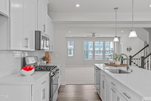 kitchen with a ceiling fan, a sink, decorative backsplash, dark wood-type flooring, and stainless steel appliances