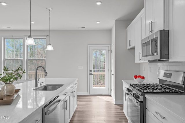 kitchen featuring wood finished floors, visible vents, a sink, decorative backsplash, and appliances with stainless steel finishes