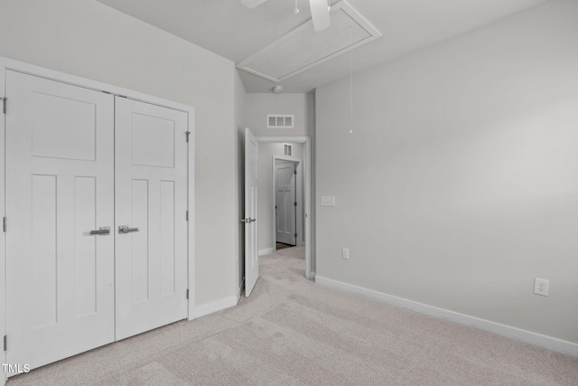 unfurnished bedroom with visible vents, baseboards, light colored carpet, attic access, and ceiling fan