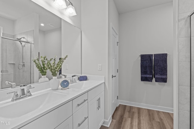 bathroom featuring a stall shower, a sink, wood finished floors, double vanity, and baseboards