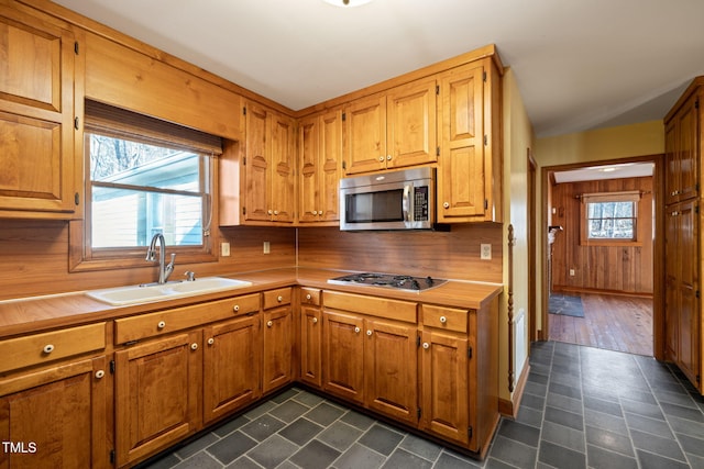 kitchen with a sink, appliances with stainless steel finishes, brown cabinetry, and light countertops