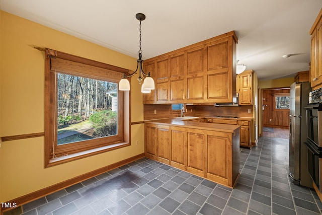 kitchen with baseboards, a peninsula, freestanding refrigerator, decorative light fixtures, and brown cabinets