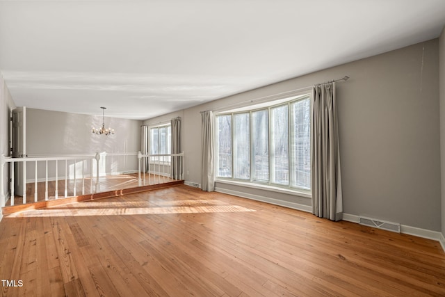 empty room featuring light wood-type flooring, visible vents, baseboards, and a chandelier