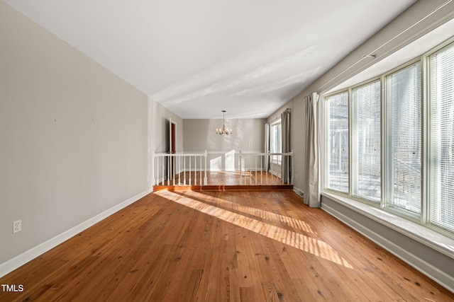 spare room featuring hardwood / wood-style flooring, a notable chandelier, and baseboards