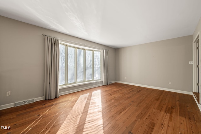 empty room featuring hardwood / wood-style floors, baseboards, and visible vents