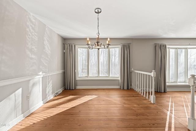 unfurnished dining area featuring an inviting chandelier, visible vents, baseboards, and wood-type flooring