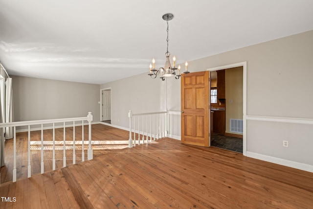 spare room featuring visible vents, baseboards, a notable chandelier, and hardwood / wood-style floors