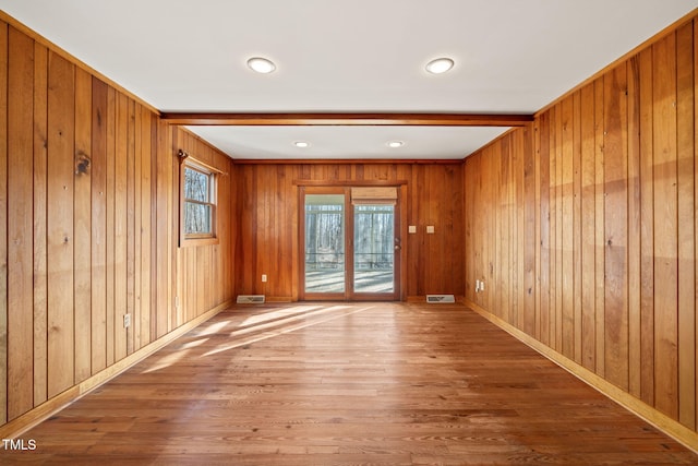 spare room with beam ceiling, wood finished floors, baseboards, and visible vents