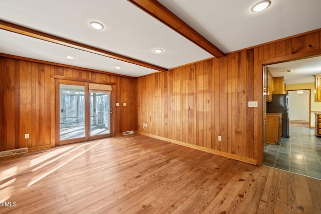 spare room featuring wooden walls, visible vents, baseboards, beamed ceiling, and wood finished floors