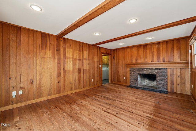 unfurnished living room with beamed ceiling, a brick fireplace, wood finished floors, and wood walls