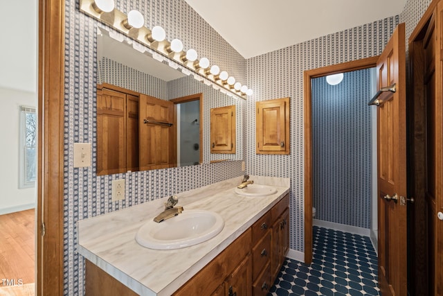 bathroom featuring a sink, lofted ceiling, double vanity, and wallpapered walls