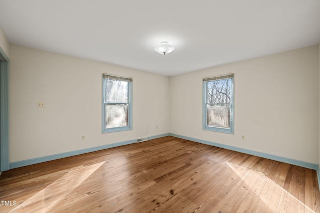 unfurnished room with hardwood / wood-style flooring, plenty of natural light, baseboards, and visible vents