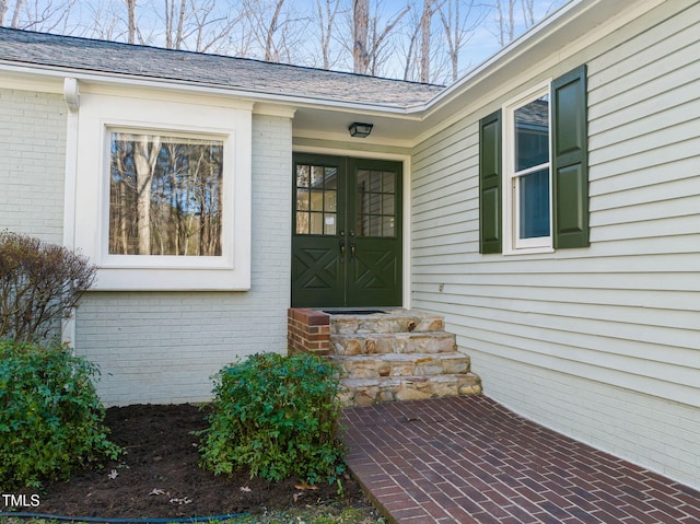 view of exterior entry featuring brick siding and a shingled roof