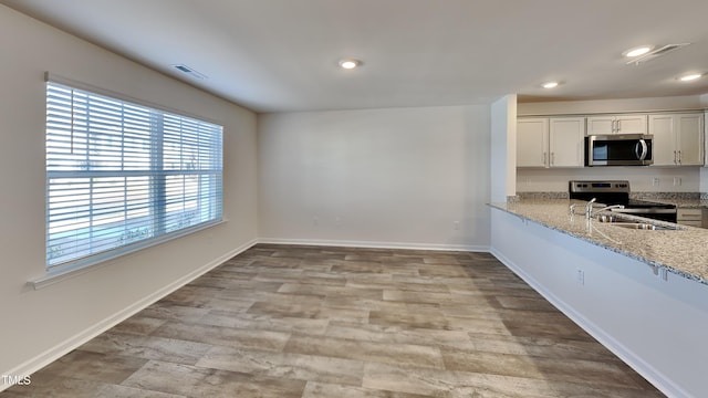 kitchen with visible vents, a sink, appliances with stainless steel finishes, baseboards, and light stone countertops