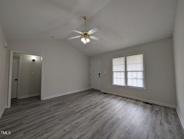 spare room featuring a ceiling fan, wood finished floors, visible vents, baseboards, and vaulted ceiling