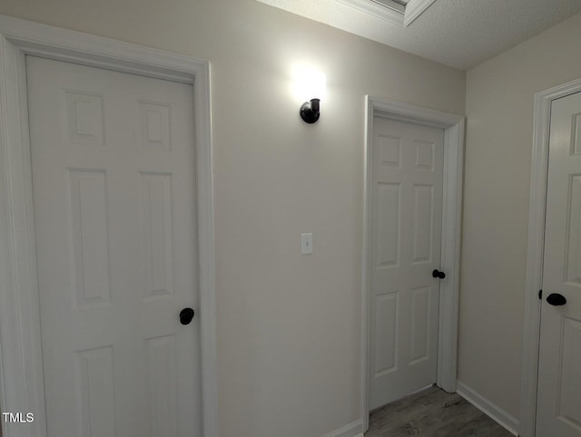 corridor with a textured ceiling, light wood-type flooring, and baseboards