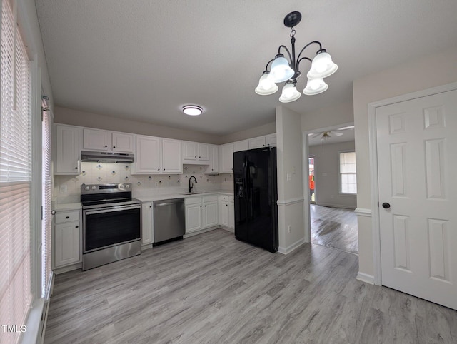 kitchen with under cabinet range hood, light countertops, appliances with stainless steel finishes, light wood-style floors, and a sink