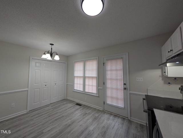 unfurnished dining area featuring visible vents, baseboards, a chandelier, light wood-type flooring, and a textured ceiling