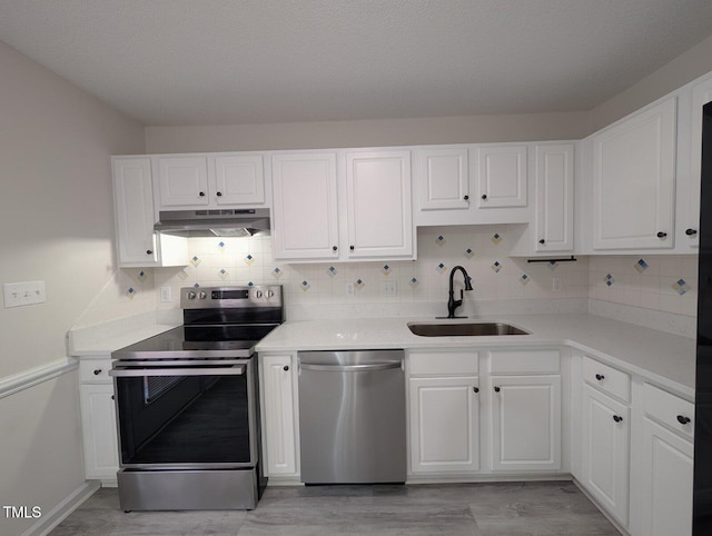 kitchen featuring under cabinet range hood, light countertops, white cabinets, stainless steel appliances, and a sink