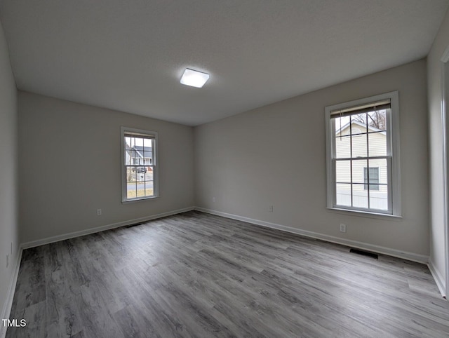 unfurnished room featuring wood finished floors, visible vents, and baseboards