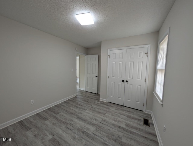 unfurnished bedroom with visible vents, baseboards, a textured ceiling, and wood finished floors