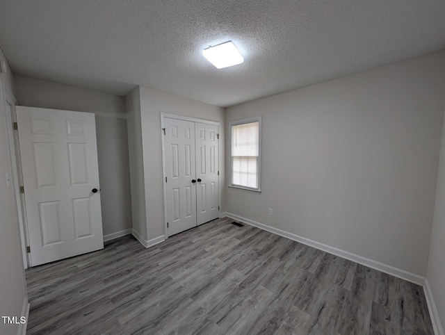 unfurnished bedroom with visible vents, a textured ceiling, wood finished floors, a closet, and baseboards