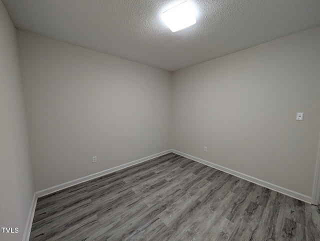 empty room featuring a textured ceiling, baseboards, and wood finished floors