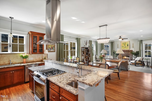 kitchen featuring a sink, ornamental molding, stainless steel appliances, a brick fireplace, and island range hood