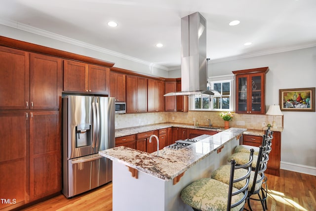 kitchen featuring island exhaust hood, a sink, light wood-style floors, appliances with stainless steel finishes, and backsplash