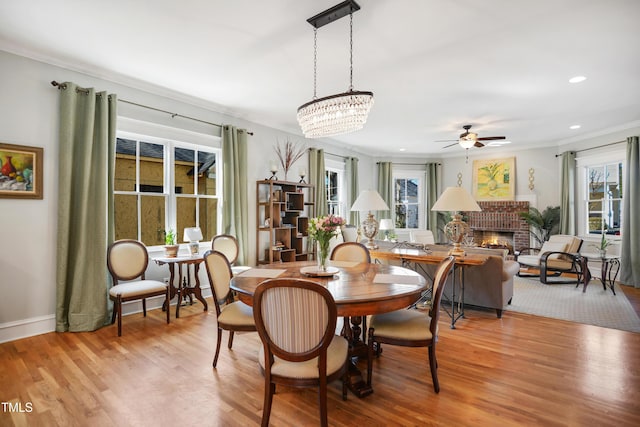 dining space with light wood-type flooring, recessed lighting, crown molding, a brick fireplace, and ceiling fan