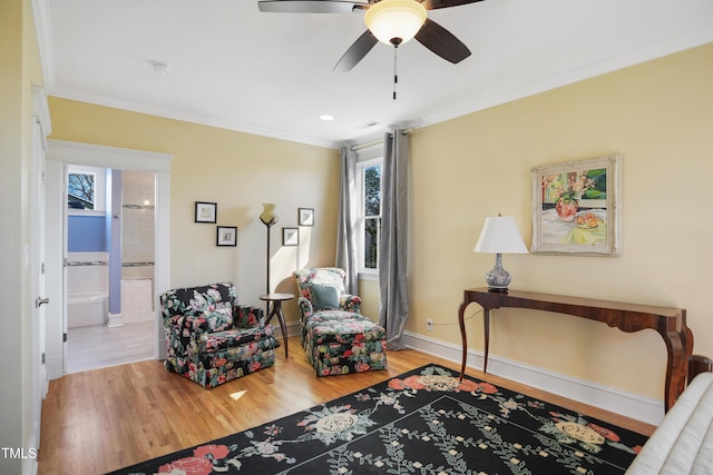 living area featuring crown molding, wood finished floors, baseboards, and ceiling fan