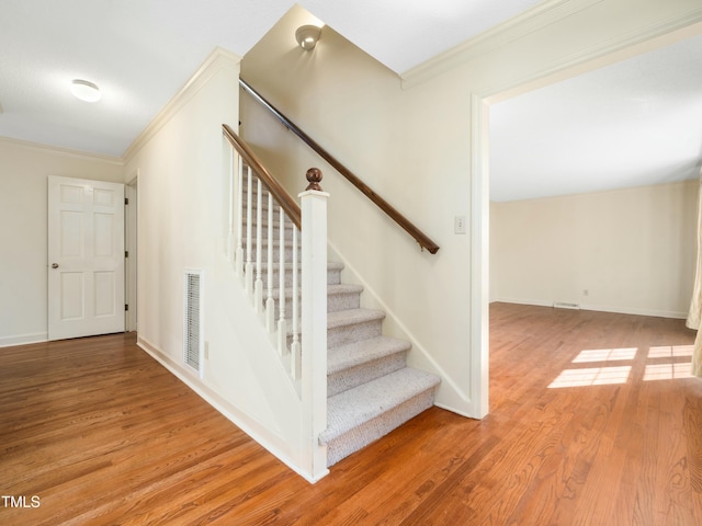 stairs featuring baseboards, wood finished floors, visible vents, and ornamental molding