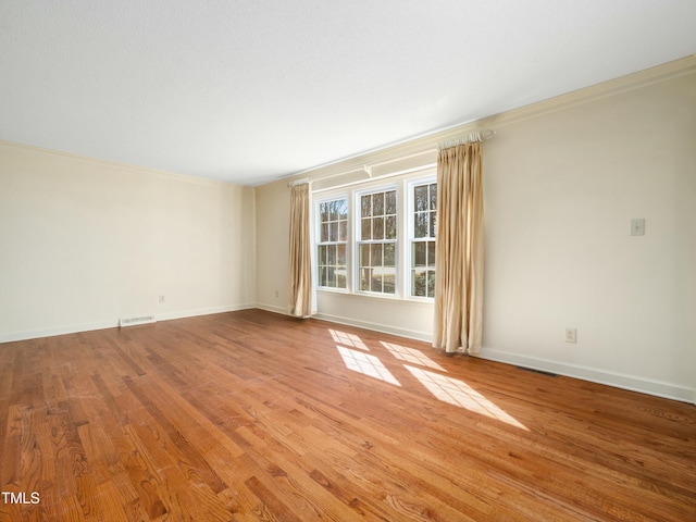 spare room with wood finished floors, visible vents, and baseboards