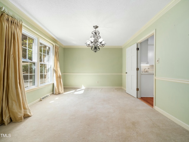 carpeted empty room featuring visible vents, crown molding, baseboards, a chandelier, and a sink