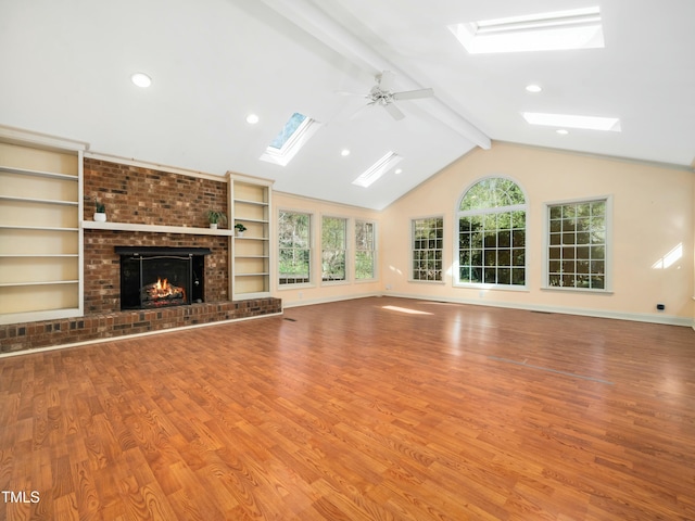 unfurnished living room featuring a brick fireplace, baseboards, vaulted ceiling with skylight, wood finished floors, and a ceiling fan